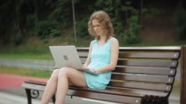 Sahilde bir dizüstü bilgisayar kullanarak bir bankta oturan bir kadın