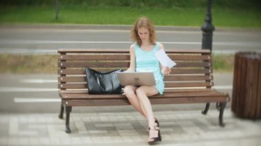 Sahilde bir dizüstü bilgisayar kullanarak bir bankta oturan bir kadın