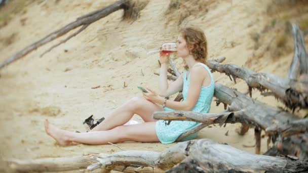 晴れた日のガラスからワインを飲んだり、海のビーチで座って呼び出しを動作するように携帯電話を拾ってビジネス紙でラップトップ コンピューターに取り組んで忙しい美しい若い女性 — ストック動画