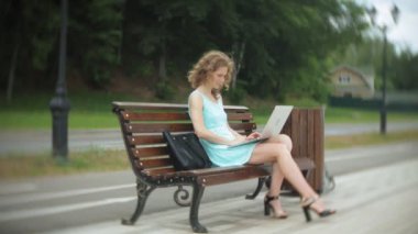 Sahilde bir dizüstü bilgisayar kullanarak bir bankta oturan bir kadın