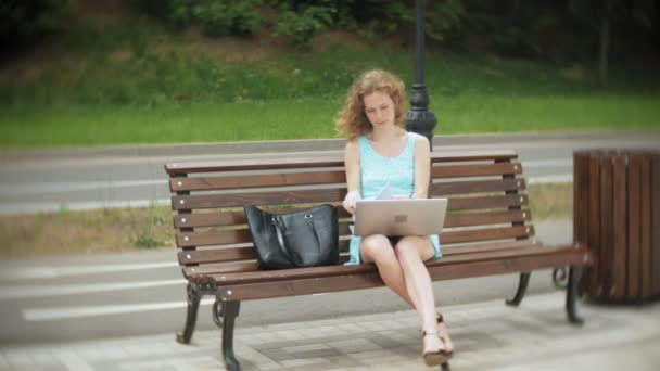 Женщина, сидящая на скамейке на пляже с ноутбуком — стоковое видео
