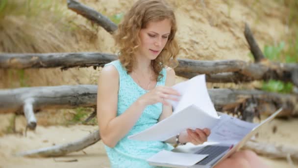 Beschäftigte schöne junge Frau, die an einem Laptop mit Geschäftspapieren arbeitet, ein Telefon zur Hand nimmt, um an einem sonnigen Tag am Strand am Meer zu sitzen und Wein aus einem Glas zu trinken — Stockvideo