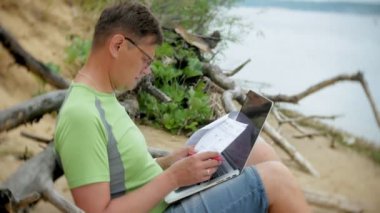 bir telefon bir güneşli gün ve içme şarap cam sahilde denizin kenarında oturan bir çağrı için malzeme çekme iş kağıtları ile bir dizüstü bilgisayarda çalışma meşgul olgun adam