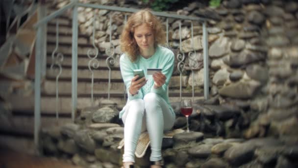 En kvinna är att använda en smartphone mot bakre vägg. Drycker och drinkar vin ur ett glas — Stockvideo