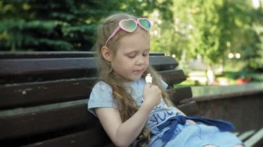 Küçük kız bir dondurma, şehir parkının arka plan yemek bir şehirde ahşap bir bankta oturmuş