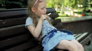 Küçük kız bir dondurma, şehir parkının arka plan yemek bir şehirde ahşap bir bankta oturmuş