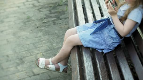 スマート フォン、都市公園の背景を使用して、都市の木製のベンチに座っている少女 — ストック動画