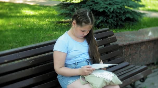 책을 읽고는, 도시 공원의 배경 도시에 나무 벤치에 앉아 어린 소녀 — 비디오