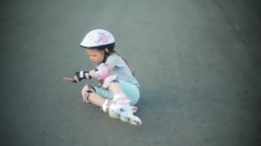 Kask ve savunma paten tekerlekli paten üzerinde küçük bir kız. Parkta silindirler üzerinde çocuk alır. Bir paten sürmek kız öğrenir.