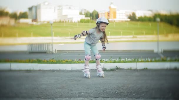 Una niña pequeña en un casco y patines de defensa en patines. El niño rueda sobre los rodillos en el parque. Chica aprende a montar un patín . — Vídeo de stock