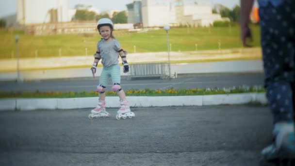 一个戴头盔的小女孩, 还有溜冰鞋上的防滑冰鞋。孩子在公园的滚筒上翻滚。女孩学会骑马溜冰. — 图库视频影像