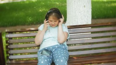 Küçük bir tablet Pc ile şişman kız ve müzik gerekse video bir yaz parkta bir bankta oturan kulaklıklar