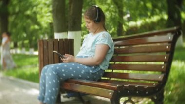 Küçük bir tablet Pc ile şişman kız ve müzik gerekse video bir yaz parkta bir bankta oturan kulaklıklar