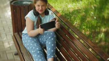 Küçük bir tablet Pc ile şişman kız ve müzik gerekse video bir yaz parkta bir bankta oturan kulaklıklar