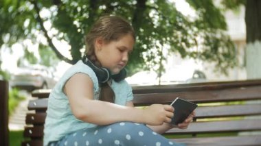 Küçük bir tablet Pc ile şişman kız ve müzik gerekse video bir yaz parkta bir bankta oturan kulaklıklar