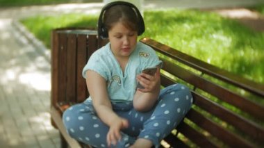 Küçük bir tablet Pc ile şişman kız ve müzik gerekse video bir yaz parkta bir bankta oturan kulaklıklar