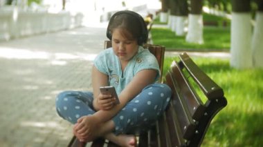 Küçük bir tablet Pc ile şişman kız ve müzik gerekse video bir yaz parkta bir bankta oturan kulaklıklar