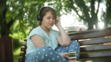 Küçük bir tablet Pc ile şişman kız ve müzik gerekse video bir yaz parkta bir bankta oturan kulaklıklar