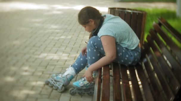 Vet meisje zittend op een bankje luisteren naar muziek kleren rolschaatsen in het park — Stockvideo