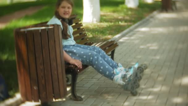 Malá tlusťoška sedí na lavičce v poslechu hudby oblečení kolečkové brusle v parku — Stock video
