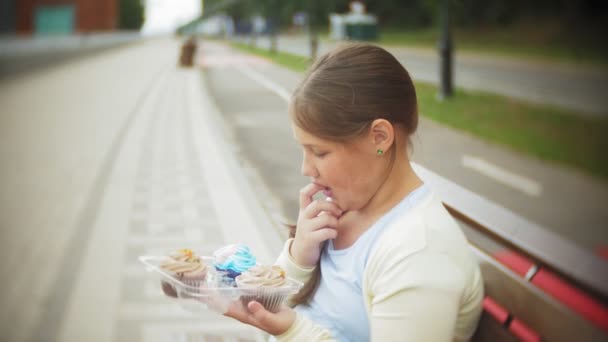 接近一个可爱的小女孩吃蛋糕, 她的手坐在公园的长凳上, 健康饮食的概念... — 图库视频影像