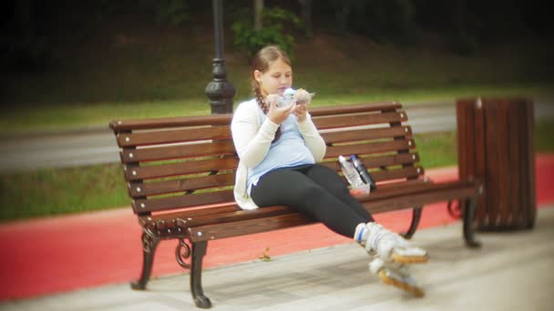 Close up de uma menina adorável comendo um bolo com as mãos sentadas em um banco no parque, o conceito de uma dieta saudável ... — Vídeo de Stock