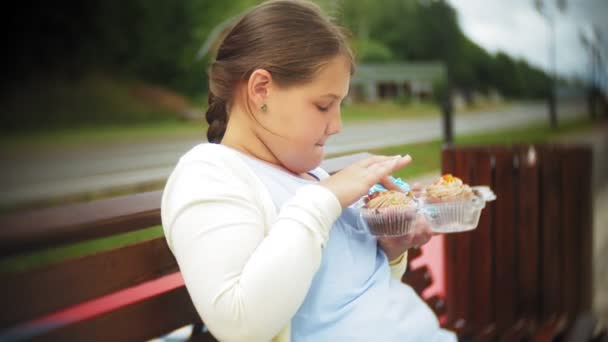 Close up de adorável menina gorda comer legumes com as mãos sentadas em um banco no parque, conceito de alimentação saudável — Vídeo de Stock