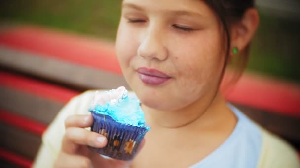 Close up de adorável menina gorda comendo um bolo com as mãos sentadas em um banco no parque — Vídeo de Stock