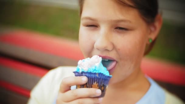 Acercamiento de adorable niña gorda comiendo un pastel con sus manos sentadas en un banco en el parque — Vídeos de Stock