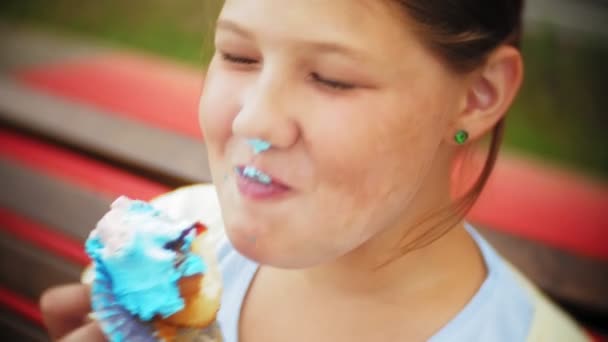 Крупним планом чарівна маленька товста дівчинка їсть торт з руками, сидячи на лавці в парку — стокове відео