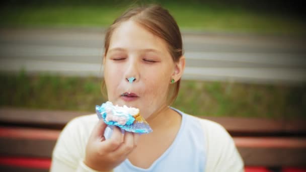 Acercamiento de adorable niña gorda comiendo un pastel con sus manos sentadas en un banco en el parque — Vídeo de stock