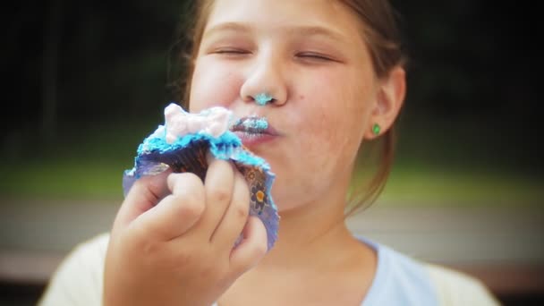 Крупным планом очаровательная маленькая толстая девочка ест торт с руками, сидя на скамейке в парке — стоковое видео