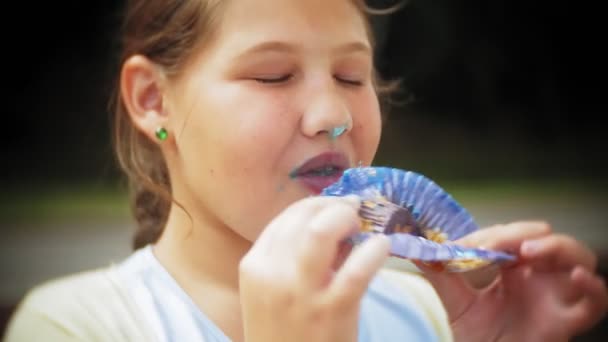 Close up de adorável menina gorda comendo um bolo com as mãos sentadas em um banco no parque — Vídeo de Stock