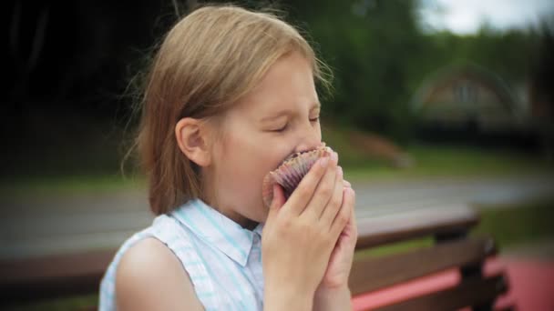 Primo piano di adorabile bambina che mangia una torta con le mani sedute su una panchina nel parco — Video Stock