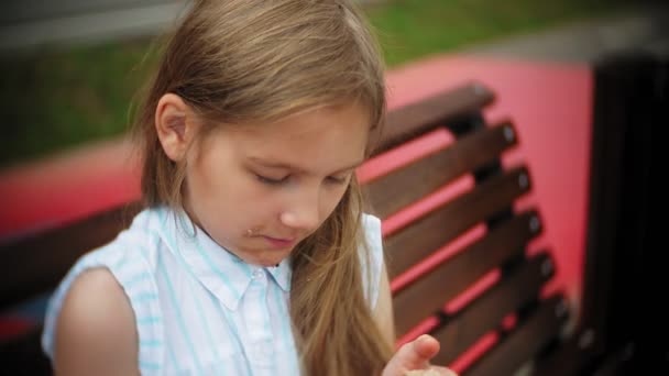 Close up van een schattig meisje, eten van een taart met haar handen zittend op een bankje in het park — Stockvideo