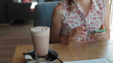 Gülümseyen ve smartphone vasıl seyir kahve içme ve kafede, rahatlatıcı mutlu kız