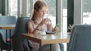 Gülümseyen ve smartphone vasıl seyir kahve içme ve kafede, rahatlatıcı mutlu kız