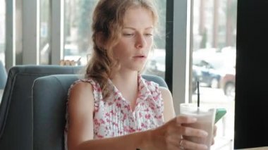 Gülümseyen ve smartphone vasıl seyir kahve içme ve kafede, rahatlatıcı mutlu kız