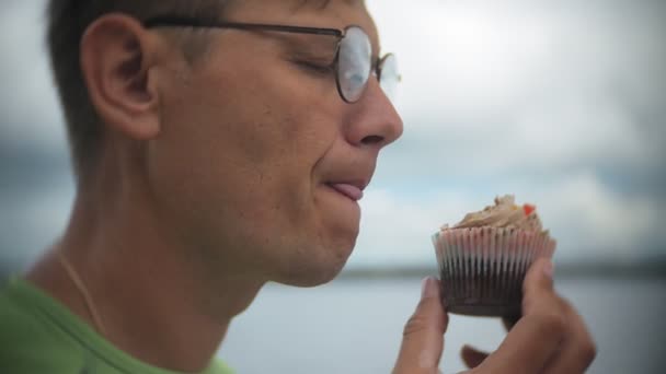 Чоловік їсть торт на вулиці, торт з шоколадом і вершками, десерт, день, жує і їсть молодого красивого чоловіка — стокове відео