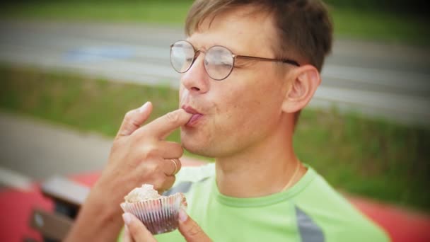 Un hombre comiendo un pastel en la calle, un pastel con chocolate y crema, postre, un día, mastica y come a un joven guapo — Vídeo de stock