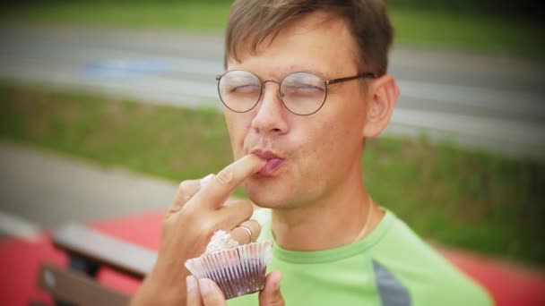 Un hombre comiendo un pastel en la calle, un pastel con chocolate y crema, postre, un día, mastica y come a un joven guapo — Vídeo de stock