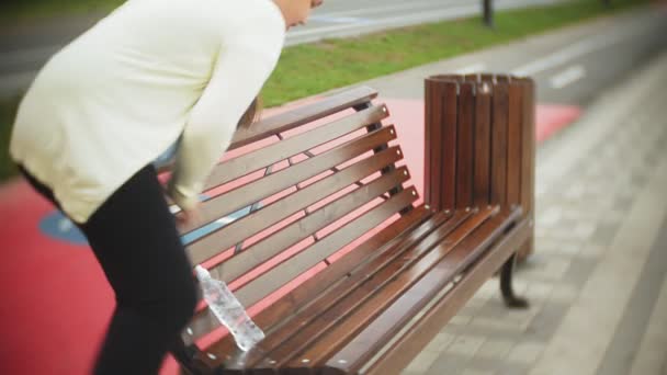 Een klein dik meisje op rollen water drinkt. Een kind drinkt water in een park op een bankje — Stockvideo