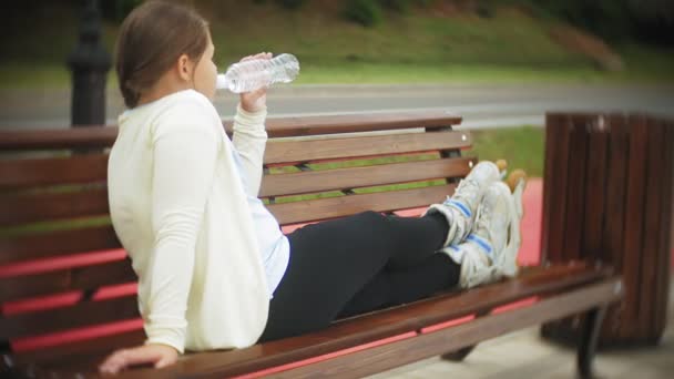 Una piccola cicciona sui rulli beve acqua. Un bambino beve acqua in un parco su una panchina — Video Stock