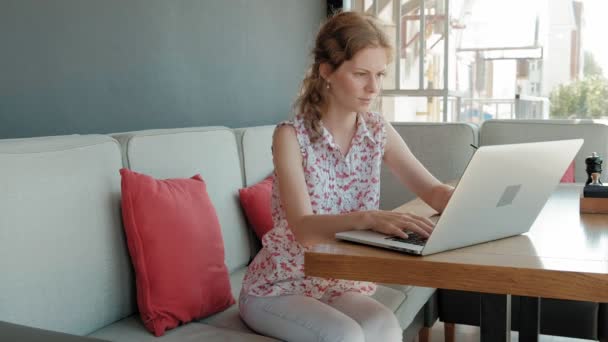 Νεαρή γυναίκα που κάθεται σε ένα τραπέζι σε ένα εστιατόριο. Μετέφερε ένα φορητό υπολογιστή με πρόσβαση στο διαδίκτυο, ελέγχει την αλληλογραφία. Μοιάζει πολύ χαρούμενος — Αρχείο Βίντεο