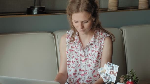 Une jeune femme d'affaires est assise à une table dans un restaurant. Elle portait un ordinateur portable avec accès à Internet, il vérifie le courrier et boire du café. Elle a l'air très heureuse — Video