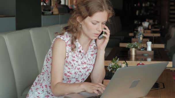 Młoda kobieta siedzi przy stoliku w restauracji. Nosiła laptop z dostępem do Internetu, sprawdza pocztę i picia kawy. Ona wygląda bardzo szczęśliwy — Wideo stockowe
