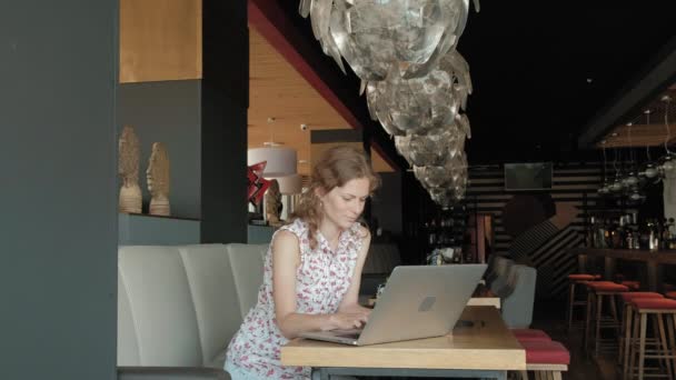 Genç iş kadını bir restoranda bir masada oturur. Kız bir laptop Internet erişimi ile yapılan, belgili tanımlık posta ve kahve içme denetler. Çok mutlu görünüyor — Stok video