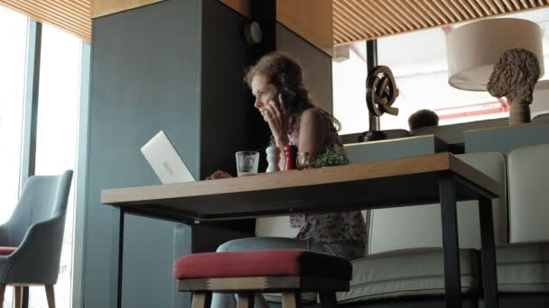 Una joven mujer de negocios se sienta en una mesa en un restaurante. Llevaba un portátil con acceso a Internet, revisa el correo y bebe café. Se ve muy feliz. — Vídeo de stock