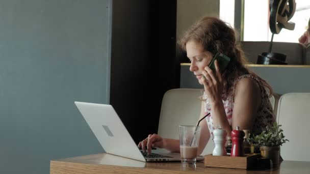 Jonge zakenvrouw zit aan een tafel in een restaurant. Ze droeg een laptop met toegang tot het Internet, het controleert de mail en koffie drinken. Ze ziet er erg blij — Stockvideo