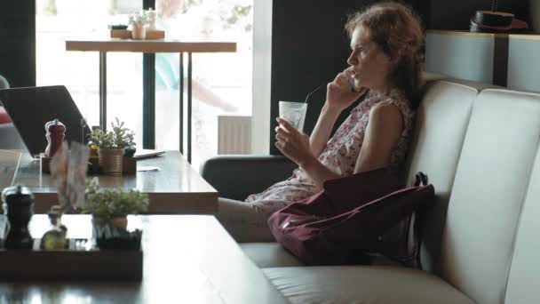 O tânără femeie de afaceri stă la o masă la un restaurant. Avea un laptop cu acces la internet, verifică poşta şi bea cafea. Pare foarte fericită. — Videoclip de stoc